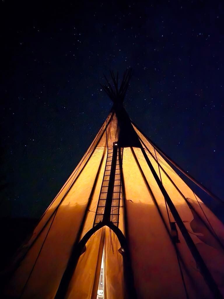 Looking up at a teepee under a starry night sky