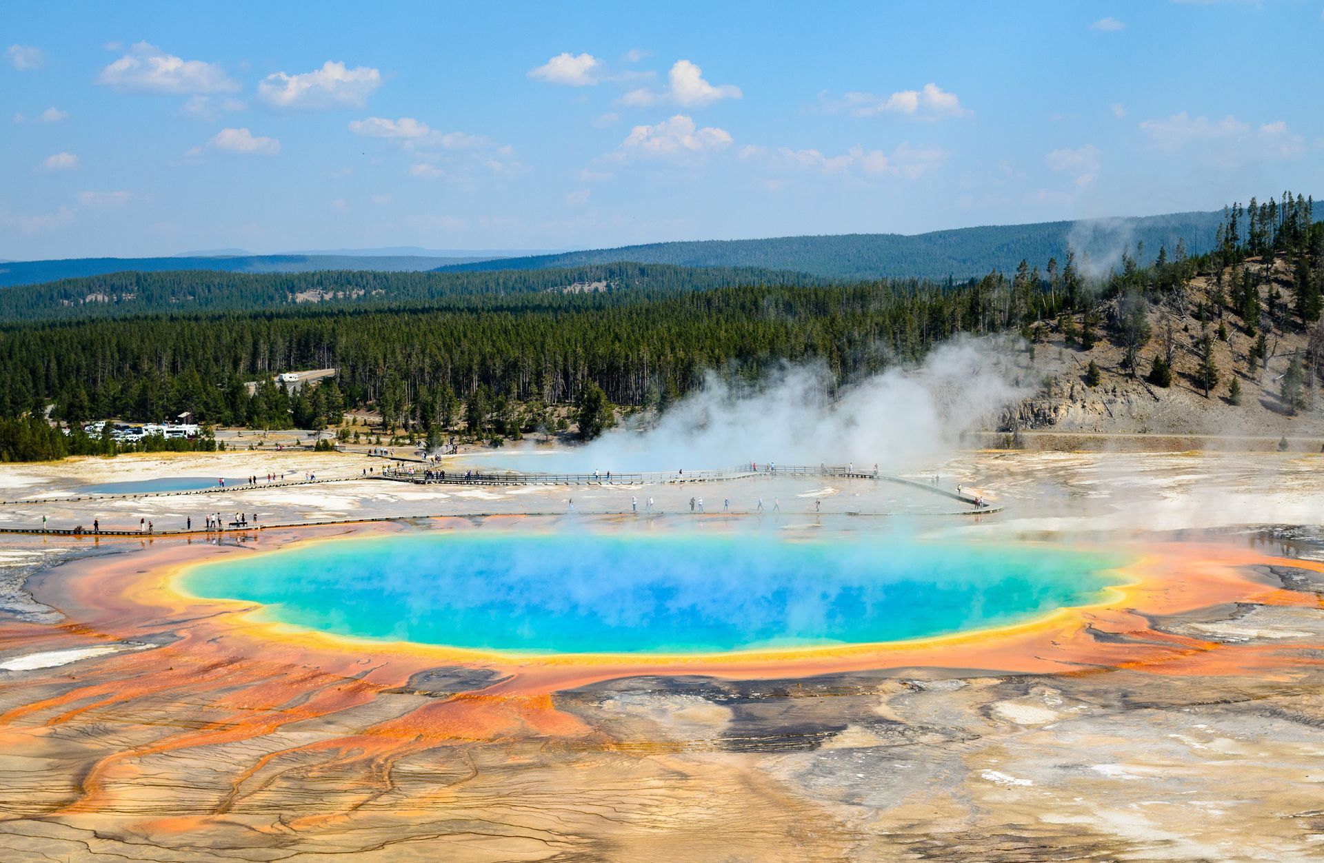A large colorful pool of water is surrounded by trees and mountains.