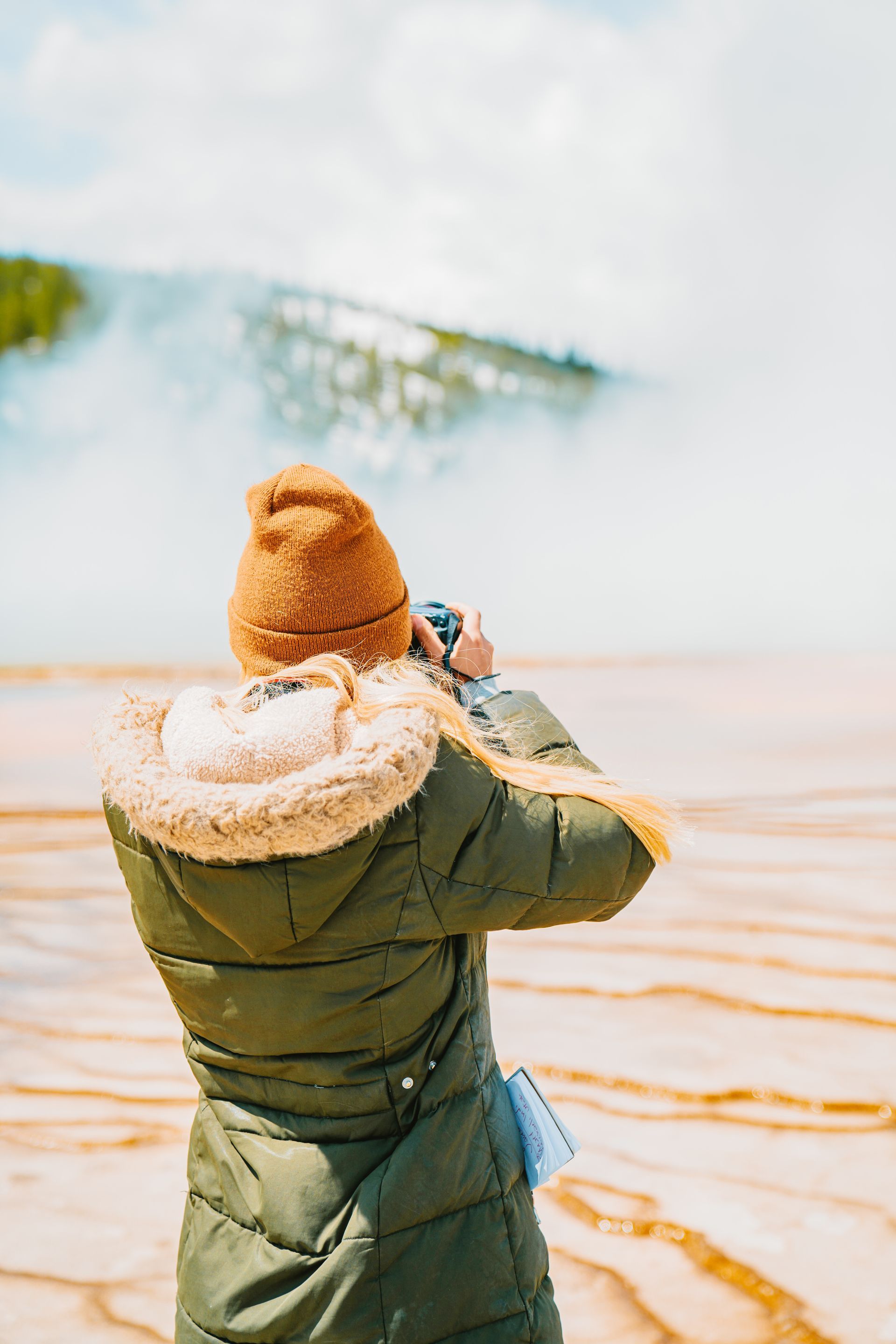 A woman is taking a picture of a waterfall with a camera.