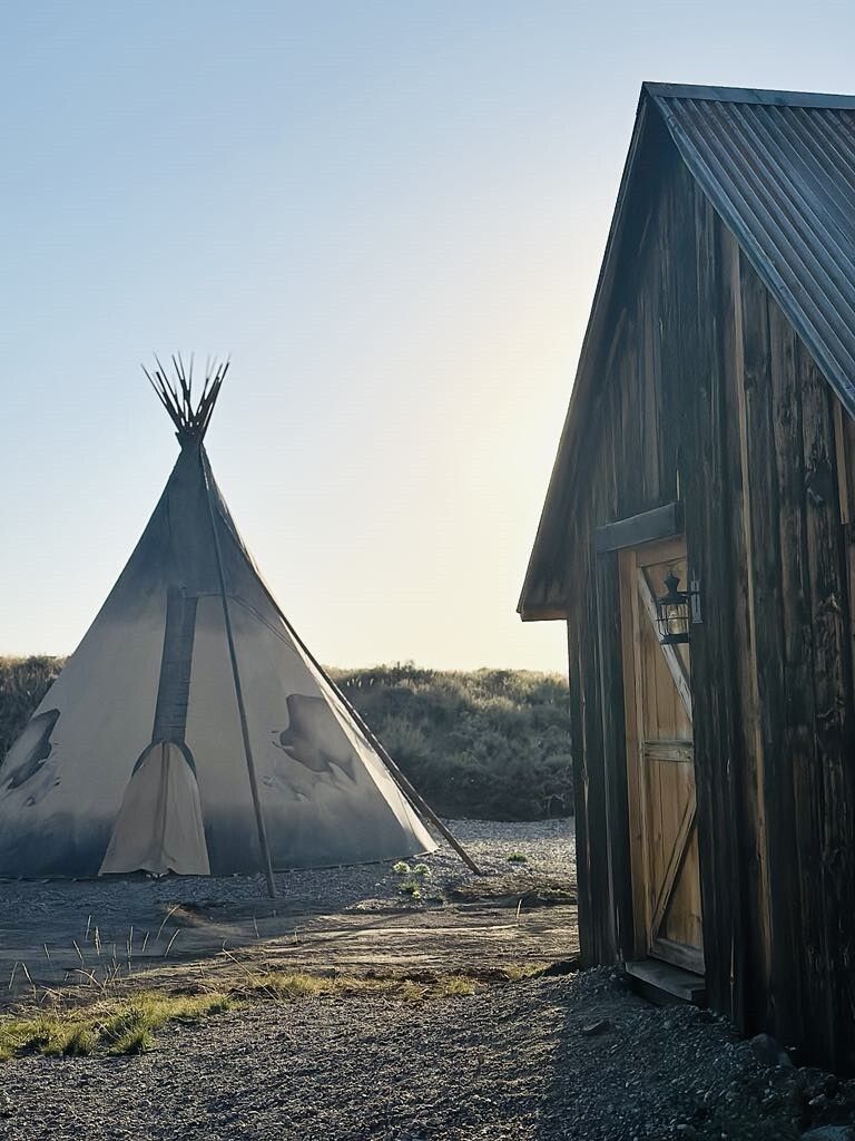 A teepee is sitting next to a small wooden building.