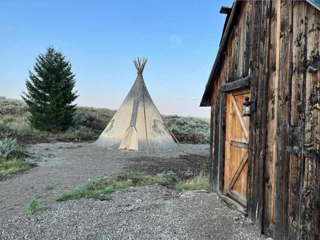 A teepee is sitting next to a wooden building.