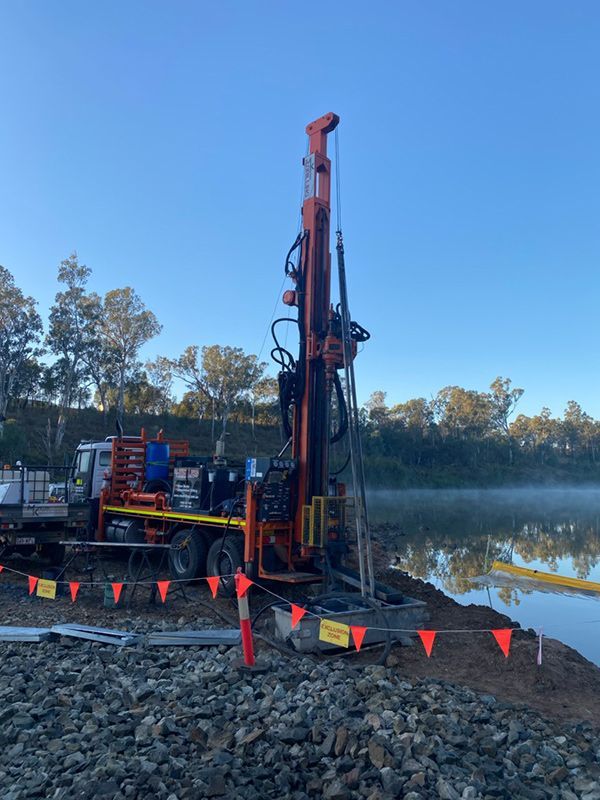 A Large Orange Machine Is Parked on Top of A Pile of Rocks Next to A Body of Water — MK Drilling in Rosemount, QLD