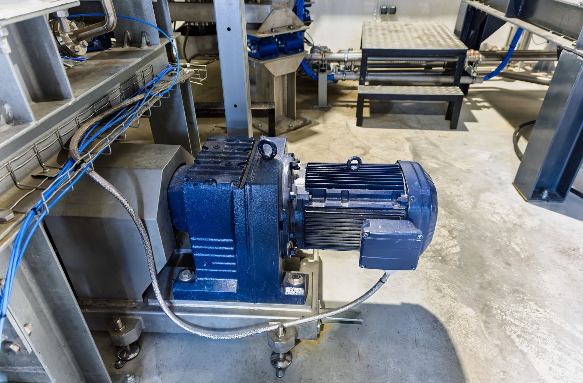 A large commercial food mixer stands near shelves holding assorted industrial motors and pumps in a warehouse.