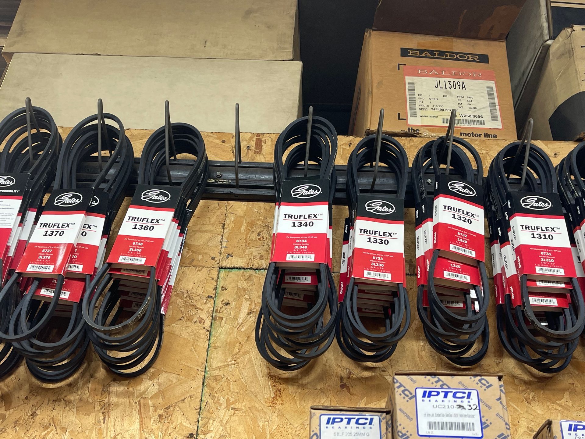 A large vertical rack filled with numerous black industrial rubber drive belts, each labeled with a small white tag.