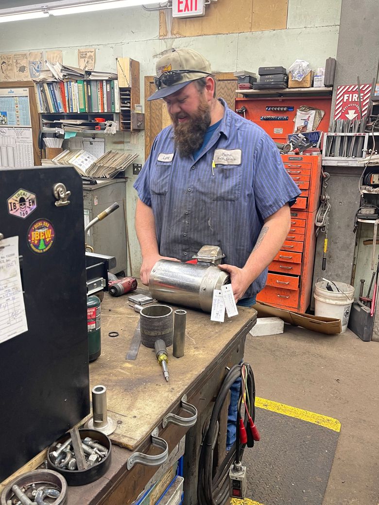 A mechanic repairs a reddish-brown electric motor on a workbench filled with tools and parts in a busy workshop. A mechanic repairs a reddish-brown electric motor on a workbench filled with tools and parts in a busy workshop.