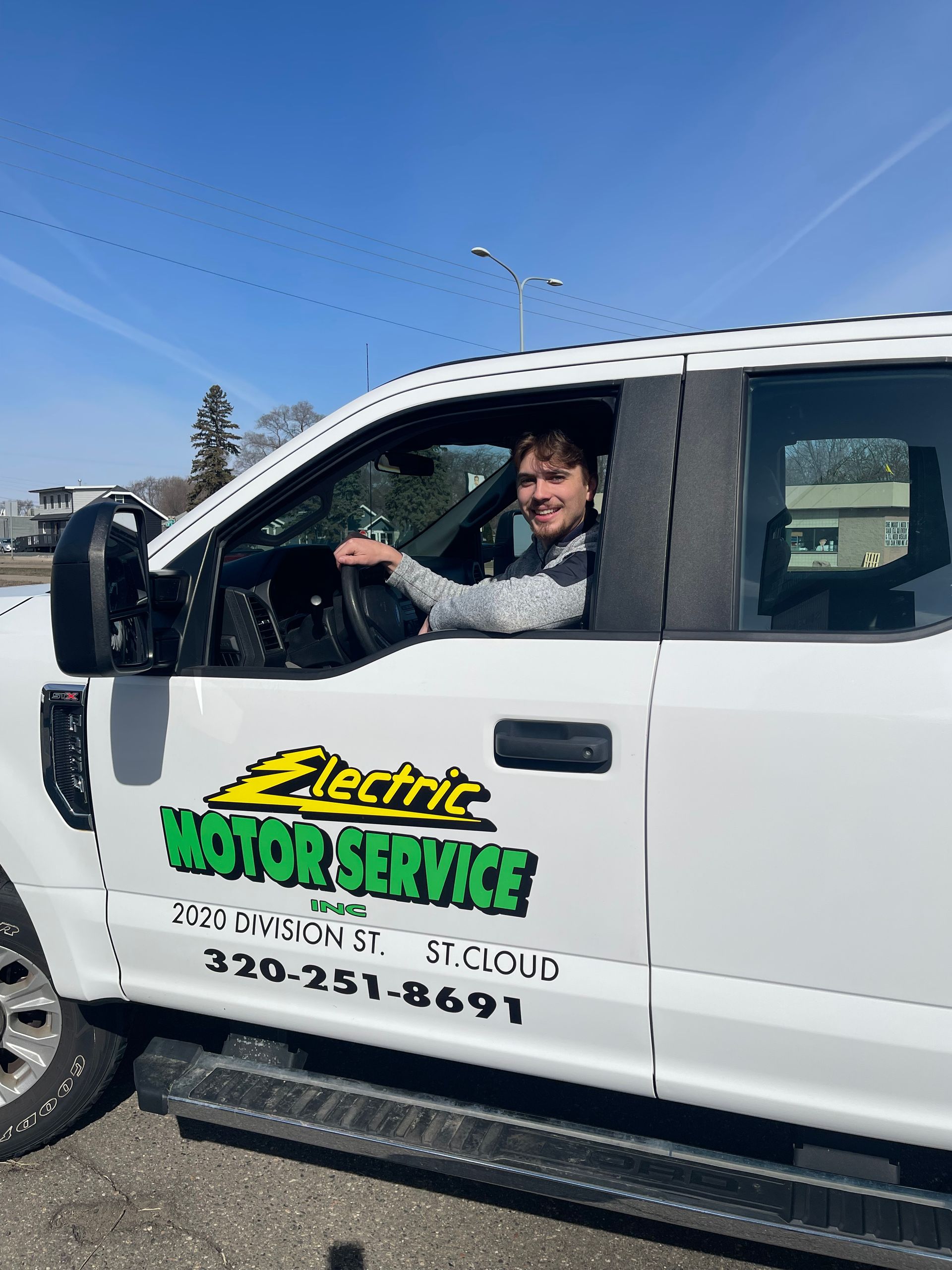 A person sits in the driver’s seat of a white service truck labeled 