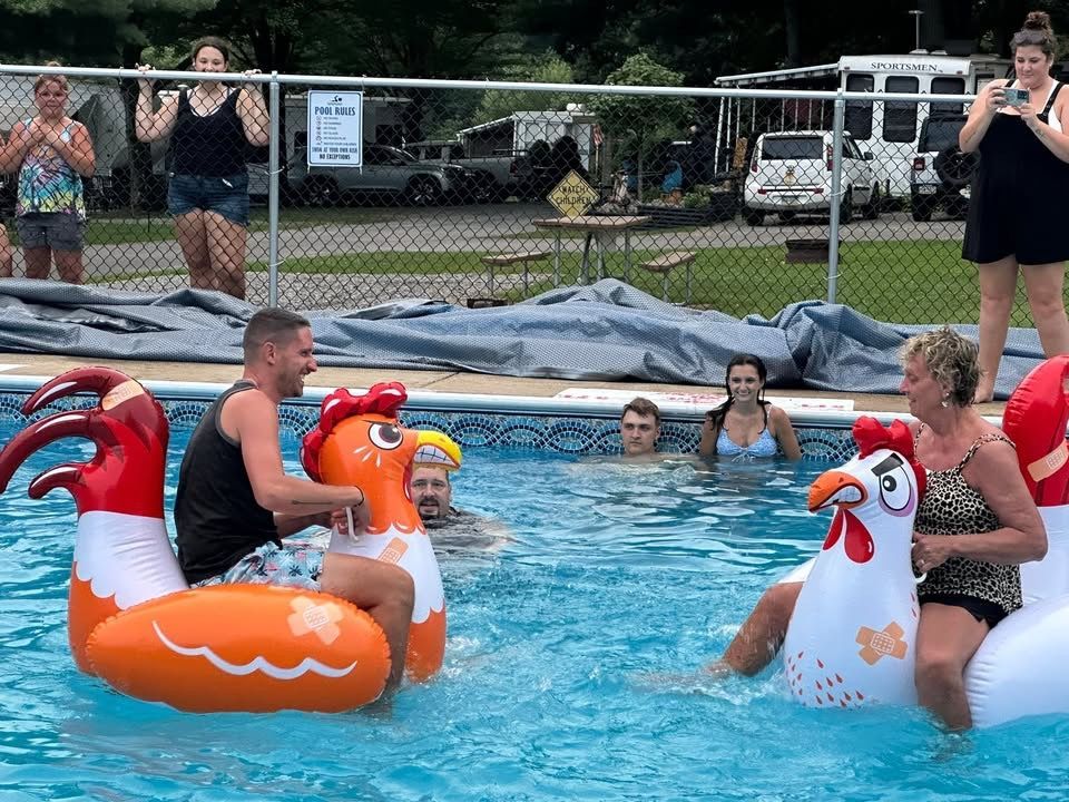 People on inflatable rooster floats in a pool, others watch from the side.
