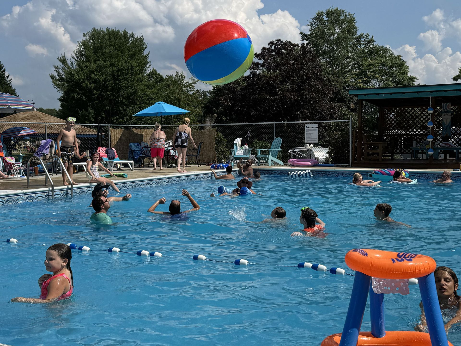 People playing in a swimming pool with a large beach ball overhead.