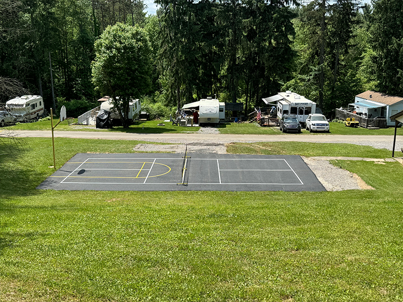 Basketball/volleyball court in grassy area, RVs parked nearby, trees in background.
