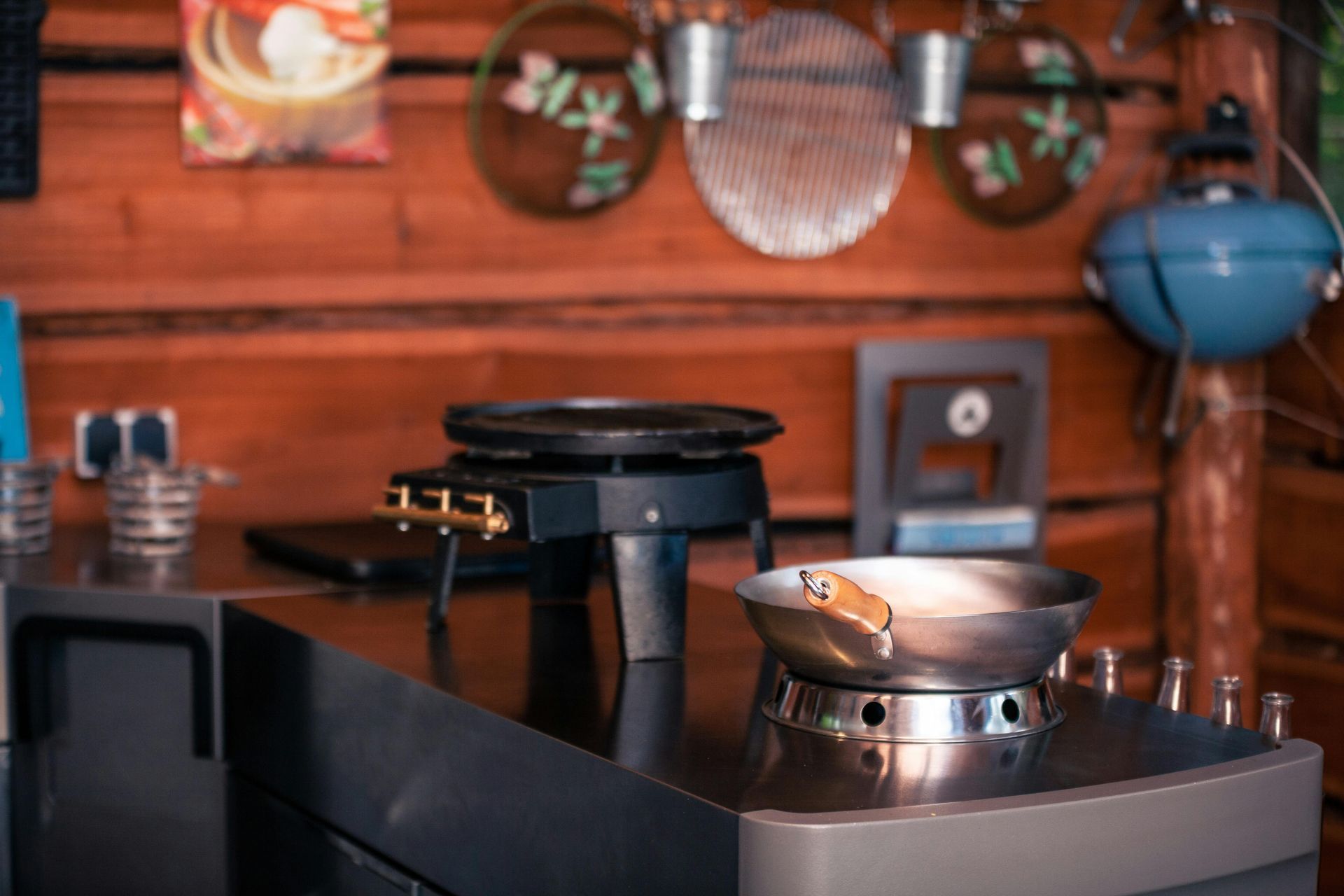 Outdoor kitchen: stainless steel countertop with a wok and griddle on burners; wood paneling in background.