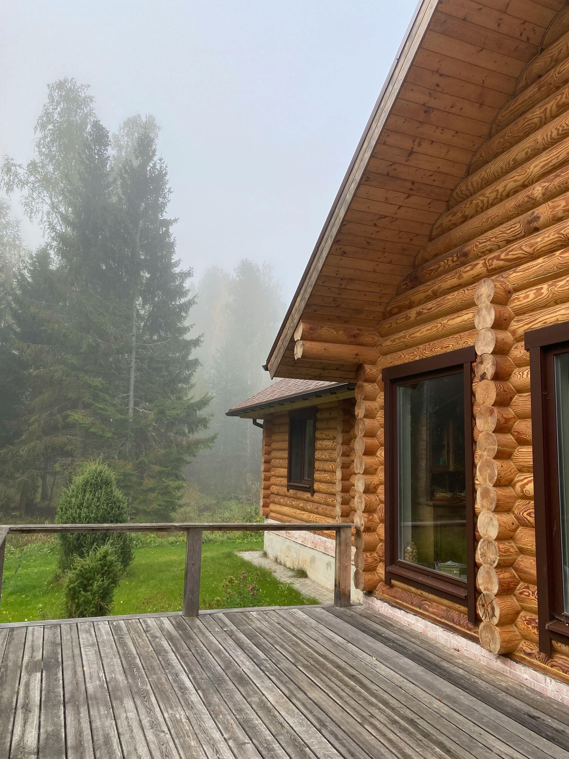 Wooden cabin with deck, in a foggy forest.