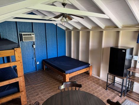 Interior of a small cabin with blue walls, bunk beds, a double bed, and a mini-fridge.