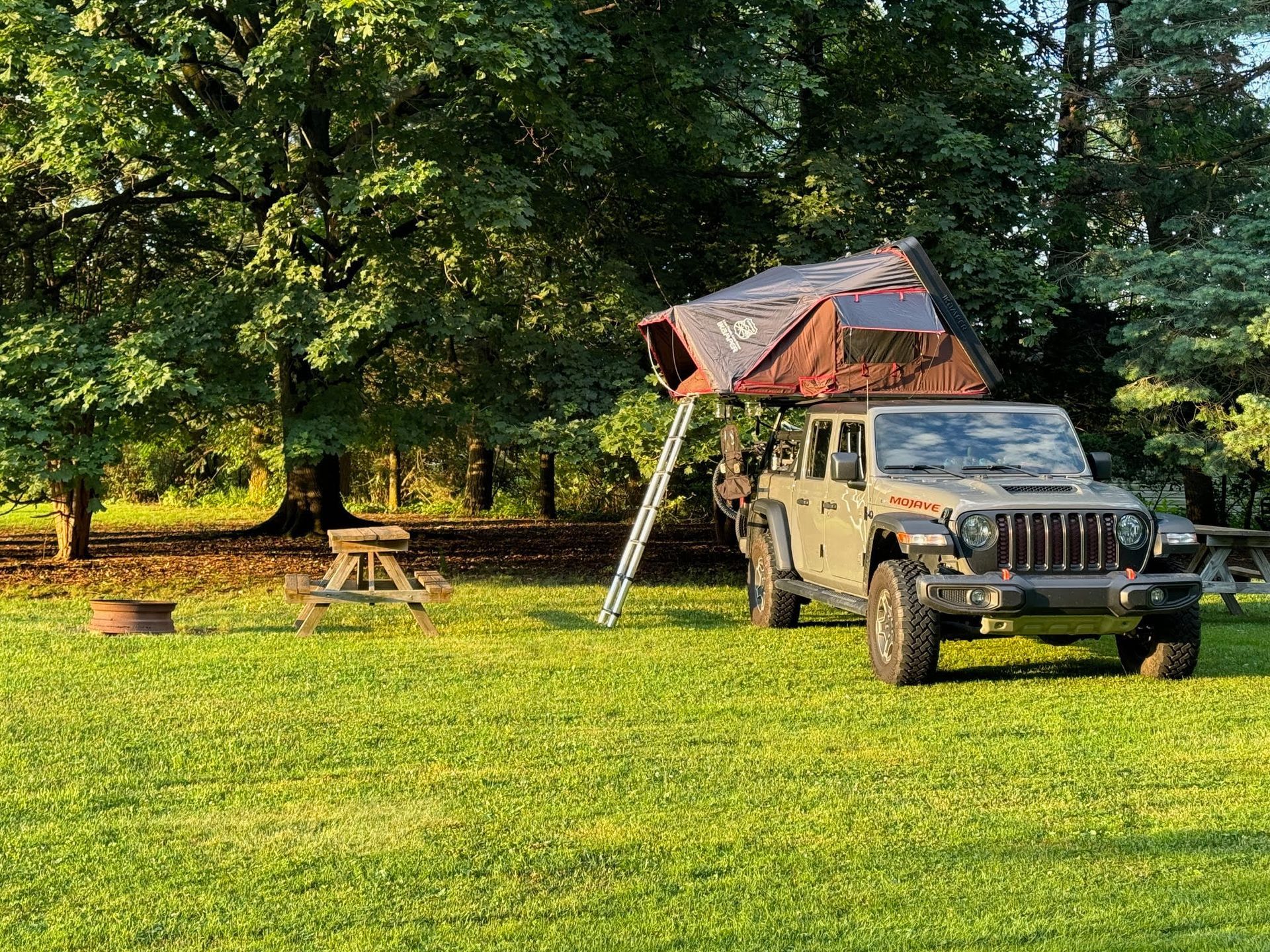 Olive green Jeep with rooftop tent set up on a grassy campsite.