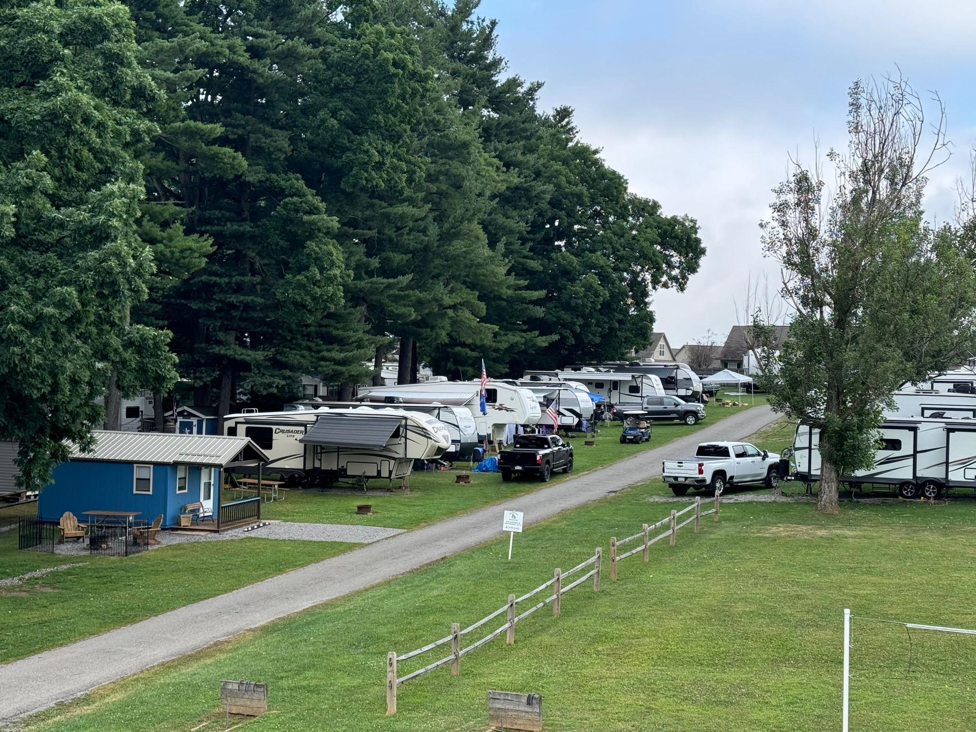 Campground scene with RVs, trees, and a dirt road.