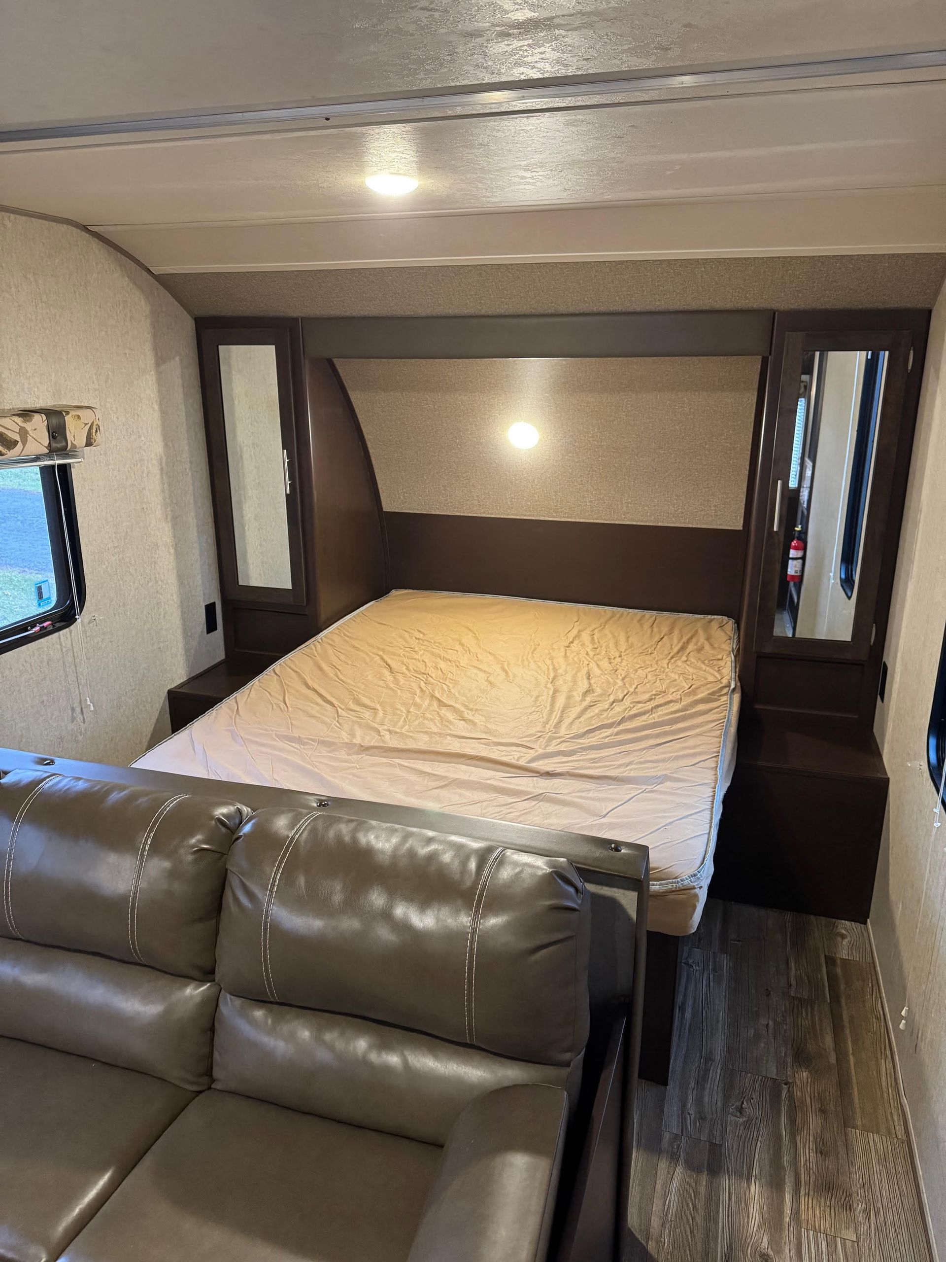 RV bedroom with bed, two mirrors, sofa, and wood flooring.