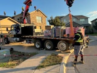 A crane lifts building materials onto a rooftop. Workers on the roof and near the truck.