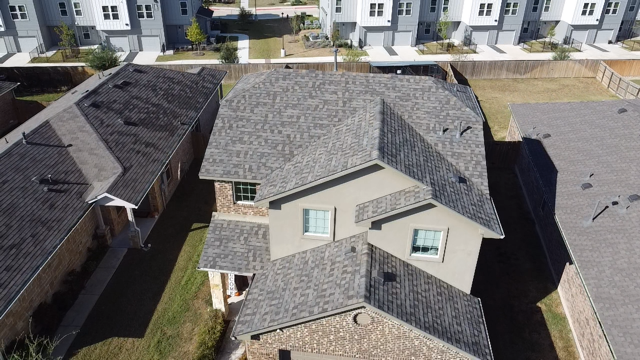Close-up of a damaged asphalt shingle roof, with debris scattered among lifted and broken shingles.