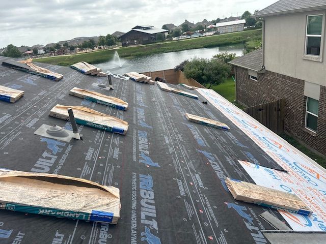 Roof under construction with black underlayment, wooden supports, and a view of a lake and neighborhood.