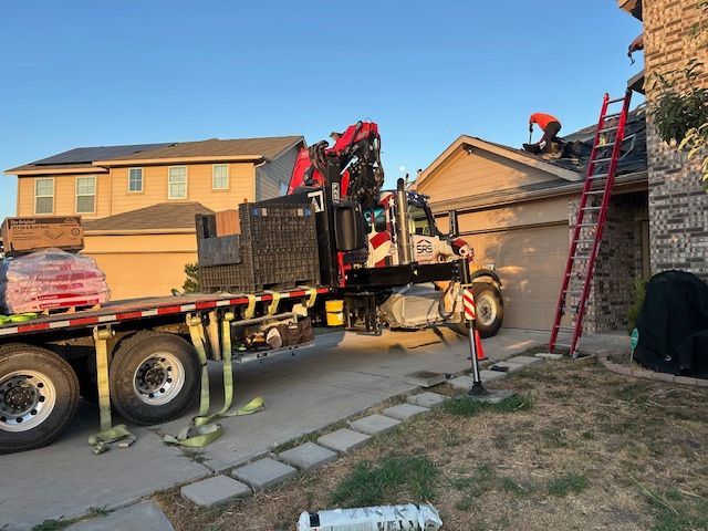 A roofing crew working on a house with a crane. Truck bed holds materials.