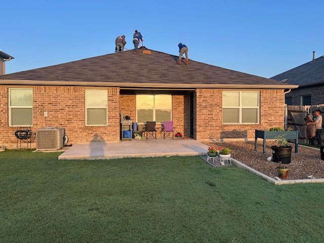 Workers on a rooftop, brick house exterior. Blue sky, green grass.