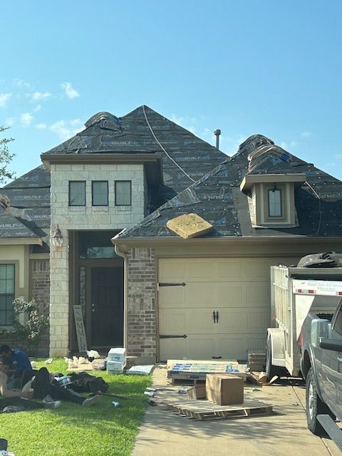 Home under construction, roof partially missing; workers on lawn, supplies visible.
