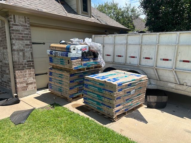 Pallets of boxed materials, next to a garage and trailer, likely for a construction project.