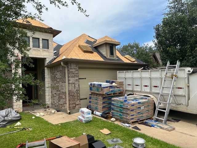 Roof of a house under construction; materials and a dumpster in the yard.