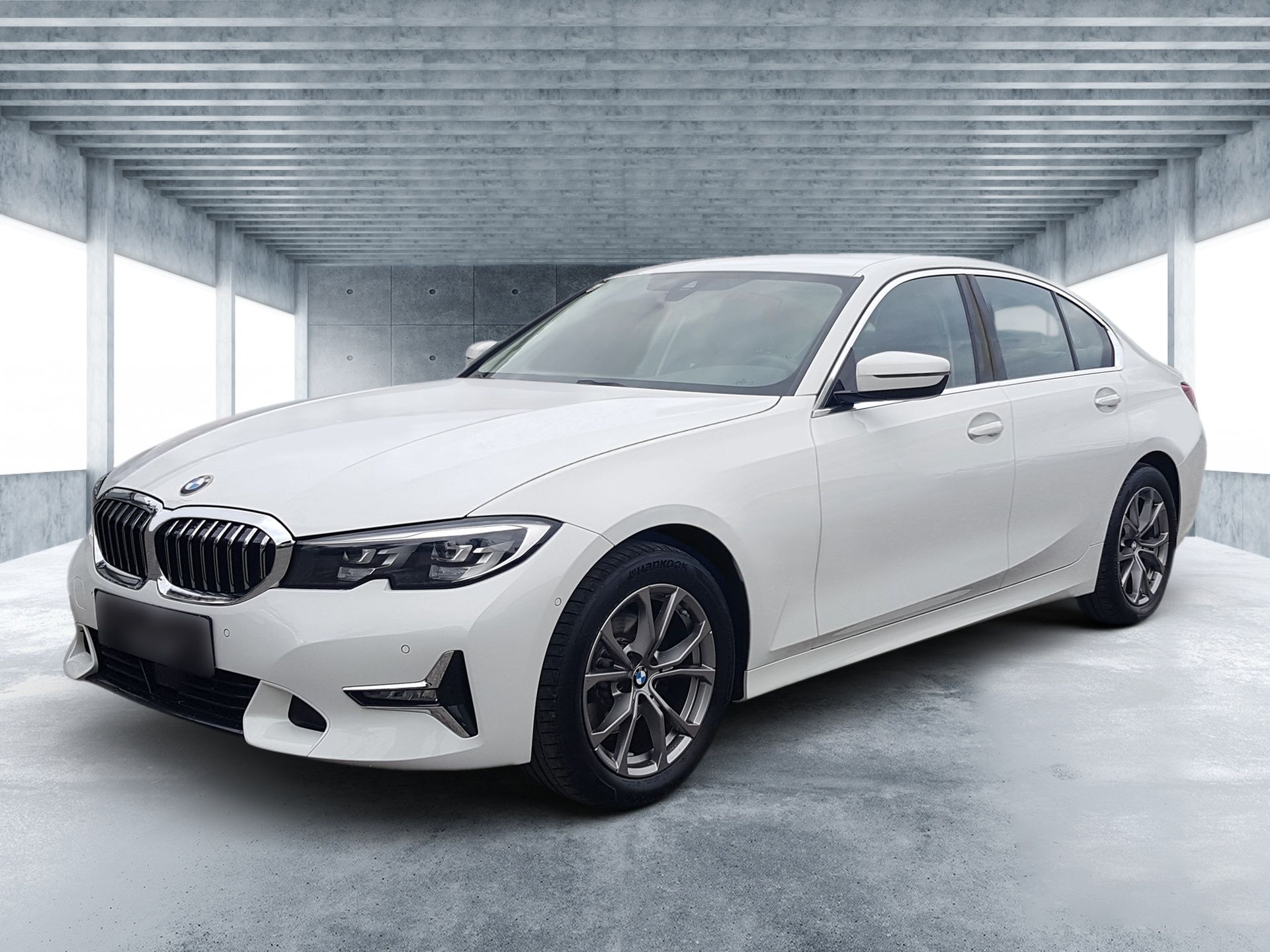 Eine weiße BMW-Limousine parkt in einer modernen Garage mit Fenstern.