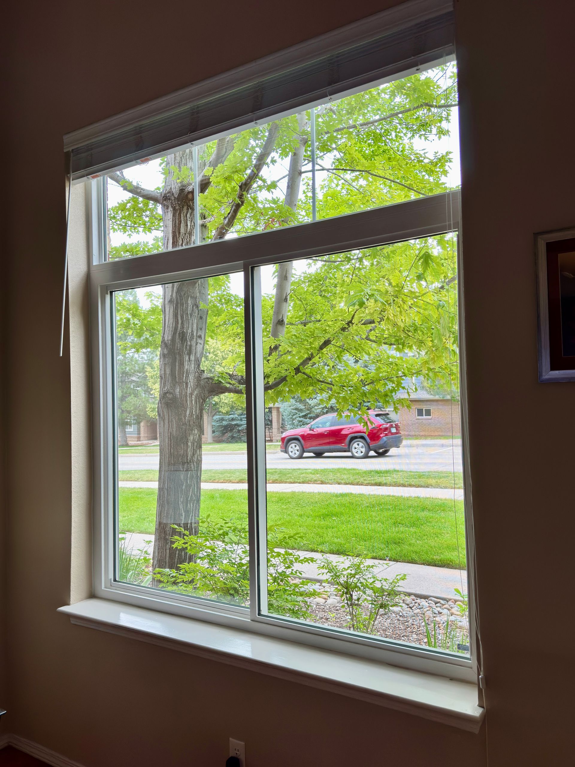 A large window with a view of a red car driving down the street.