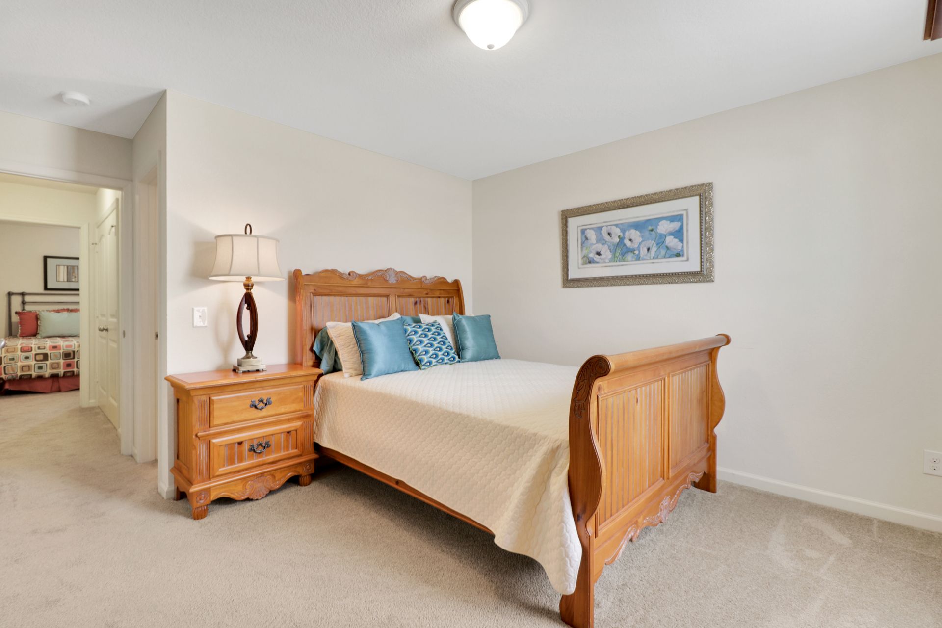 A bedroom with a bed , nightstand , lamp and picture on the wall.