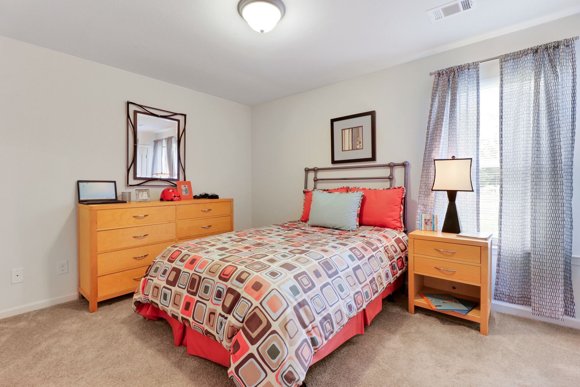 A bedroom with a bed , dresser , nightstand and mirror.