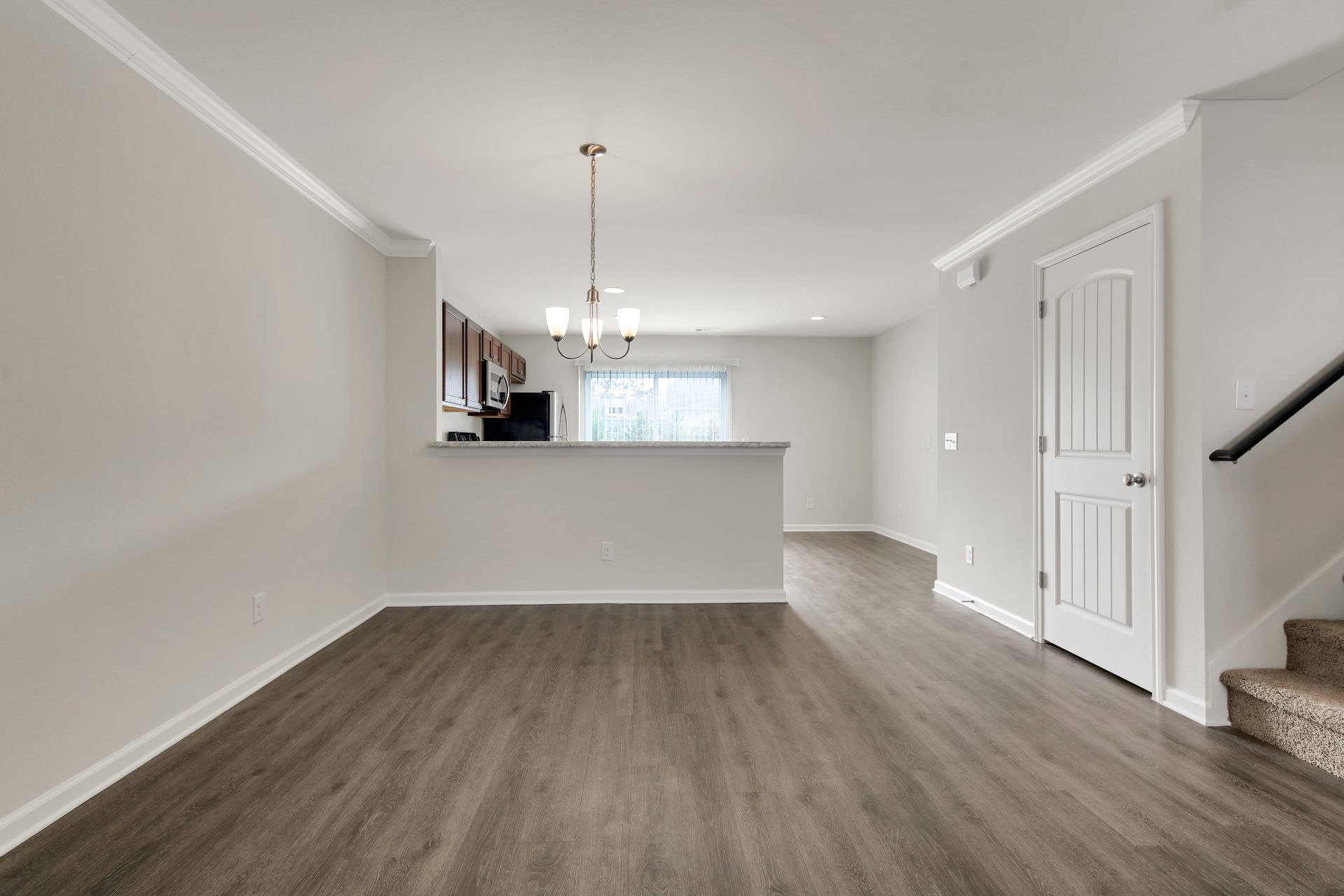 An empty living room with hardwood floors and a kitchen in the background.