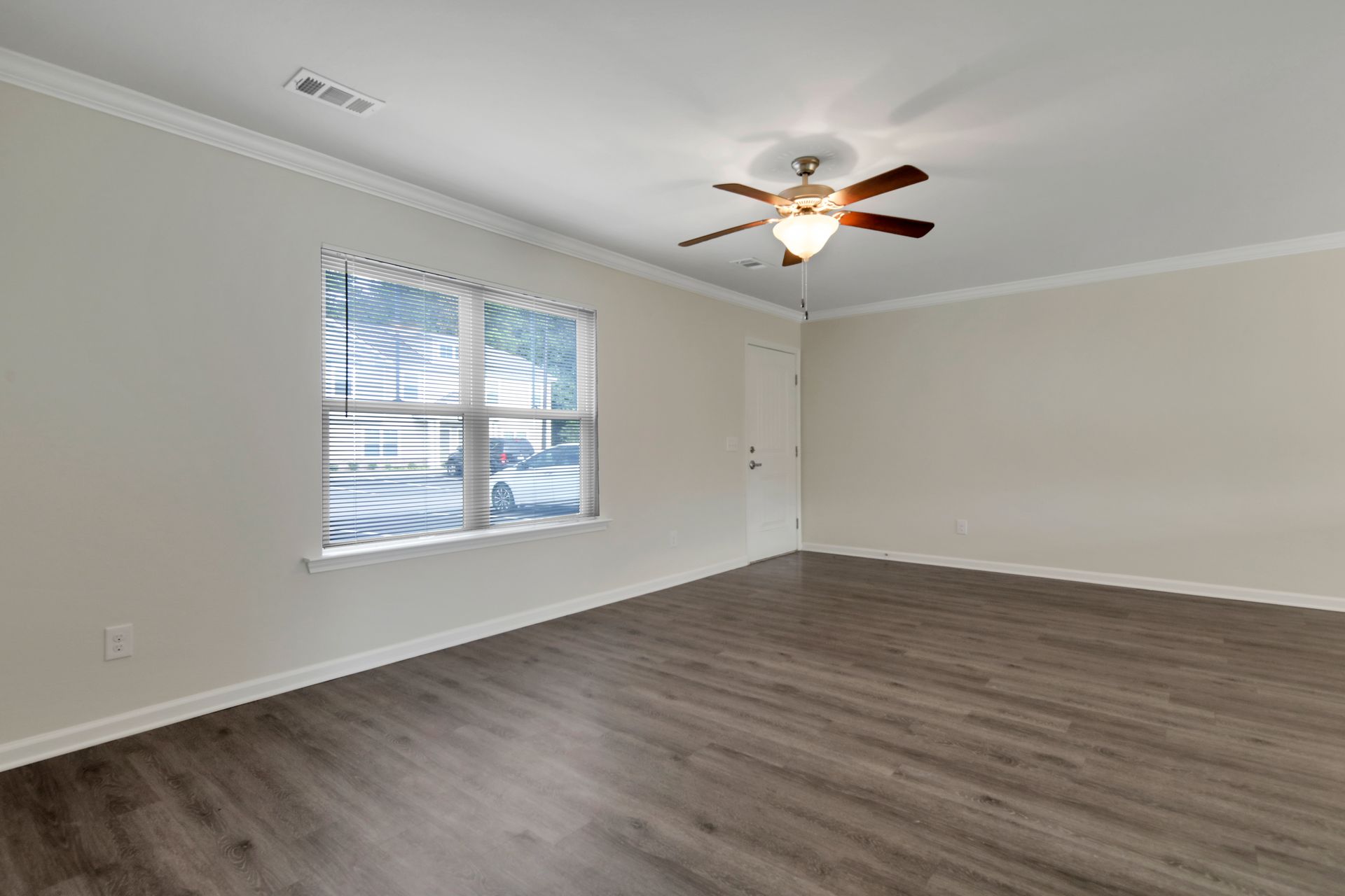 An empty living room with a ceiling fan and a window.