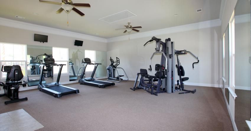 A gym with treadmills , exercise bikes , and a ceiling fan.
