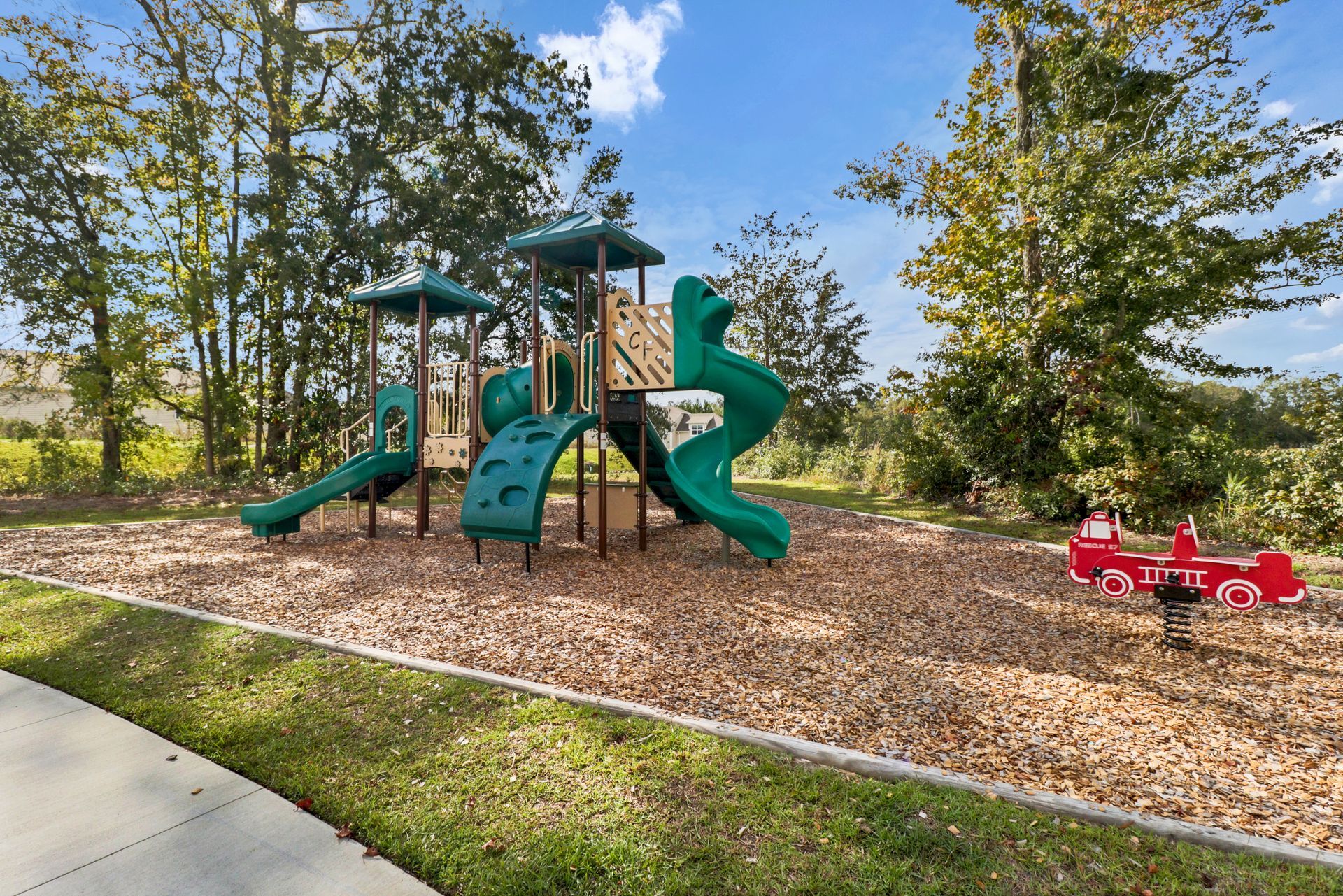 A playground with a green slide and a red car in a park.
