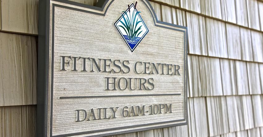 A sign on the side of a building that says fitness center hours.