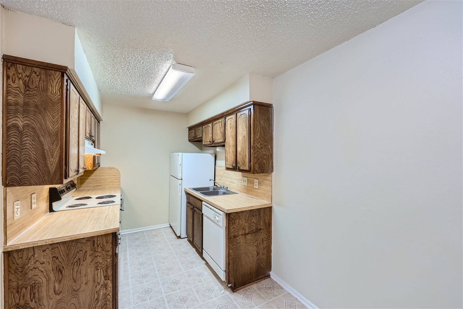 This Copperstone Point apartment kitchen has a galley-style layout with wood cabinets, beige countertops, a sink, range, fridge, and dishwasher.