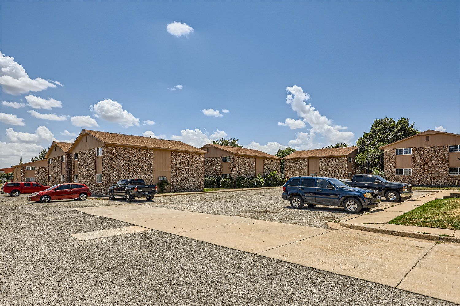 This Copperstone Point apartment community shows multiple buildings with parked cars and a blue sky.