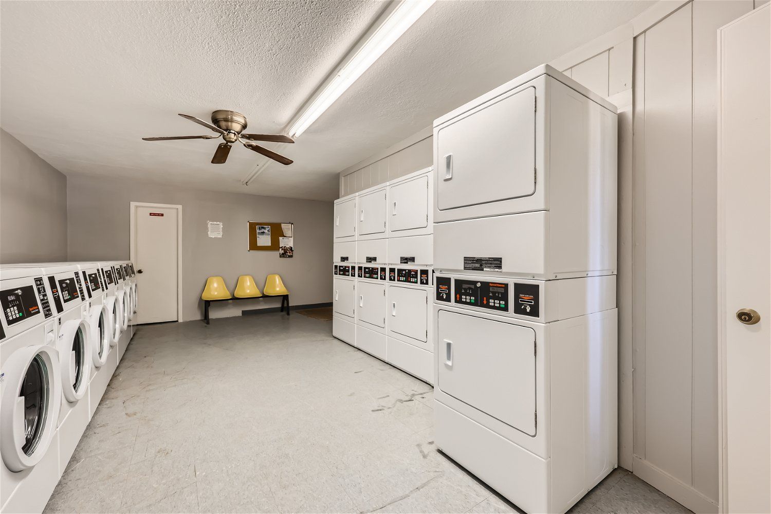 Cooperstone Pointe community laundry room with row of front-loading washers and stacked dryers, and yellow chairs.