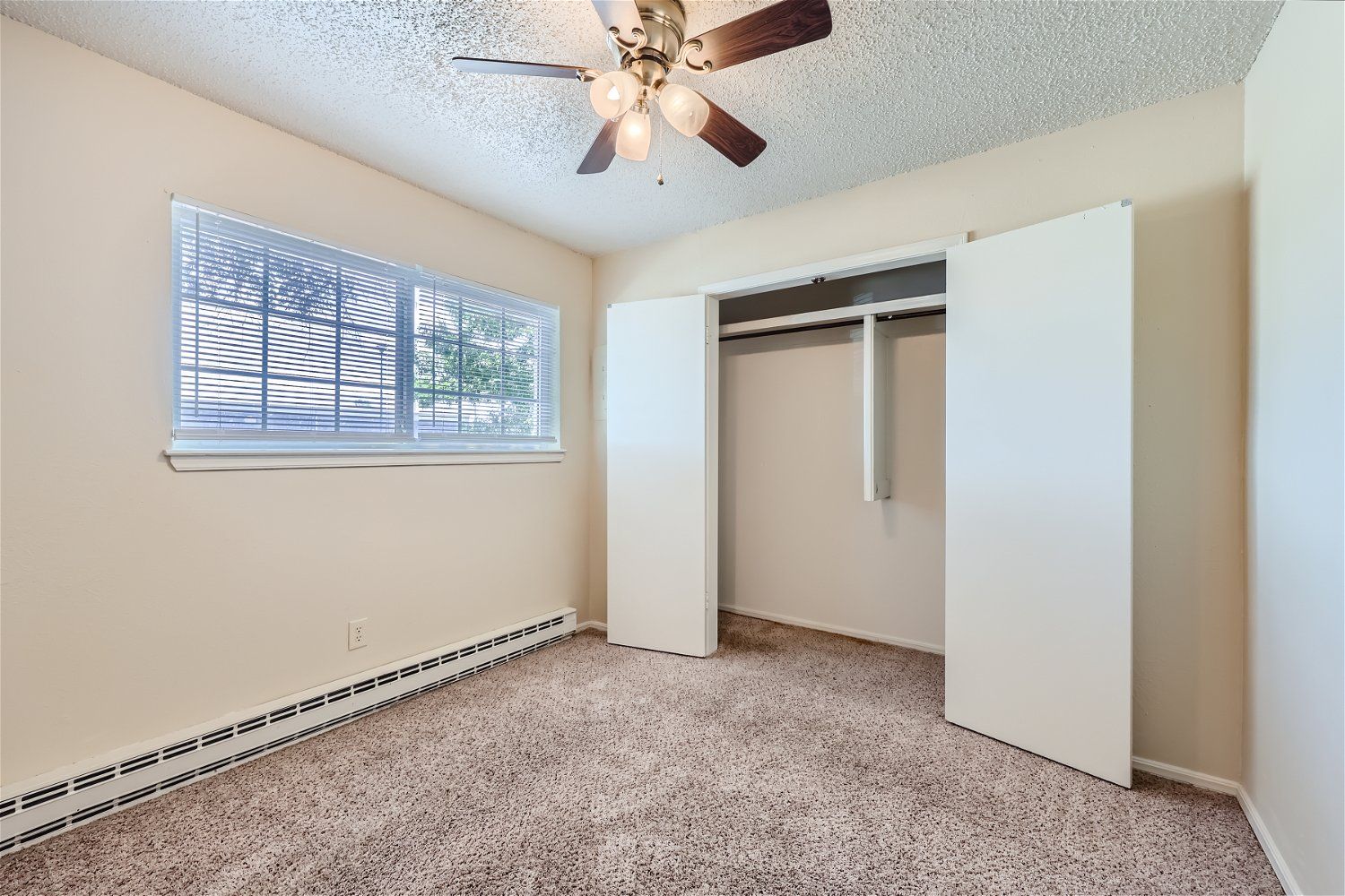 This Copperstone Point bedroom interior has a ceiling fan, beige walls, and an open double-door closet.