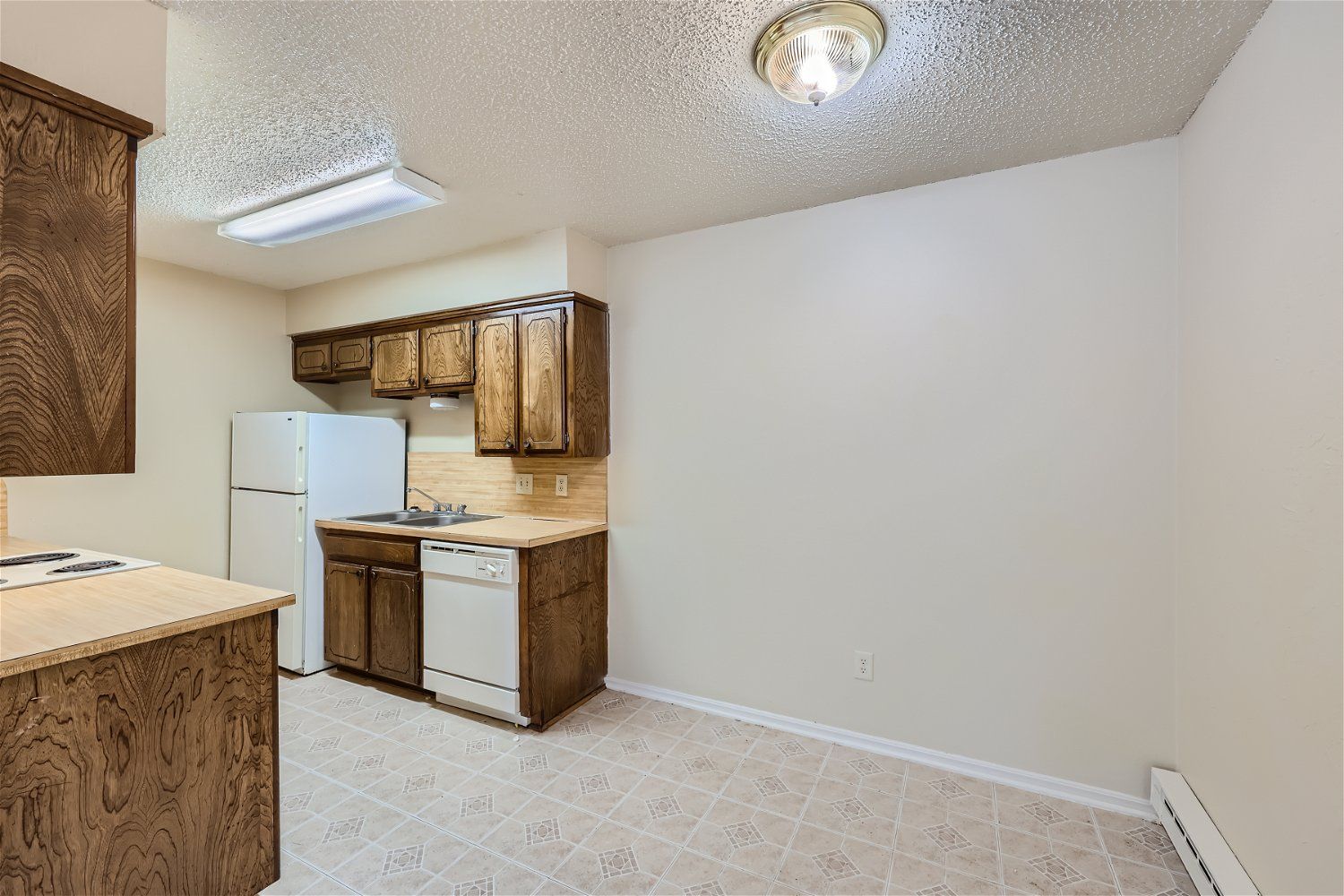 A Copperstone Kitchen in an apartment with dark wood cabinets, white appliances including fridge, stove, and dishwasher.k