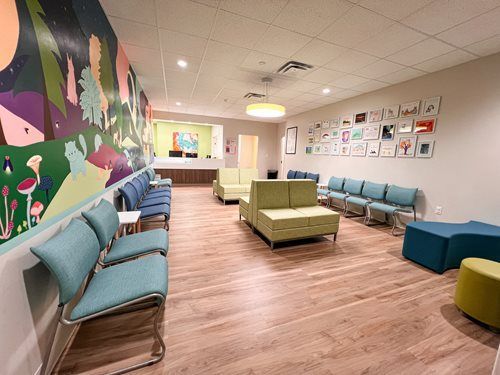 A colorful waiting room with various seating, a wall mural, and artwork. Wooden floor.