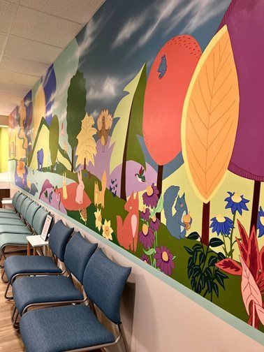 Waiting room with whimsical forest mural, blue chairs, and a pale green wall.