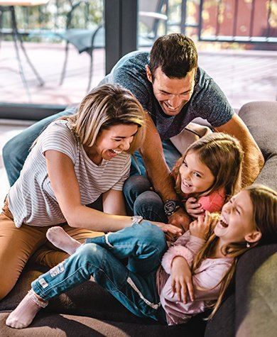 Family tickling and laughing on a couch. Living room setting with sunlight.
