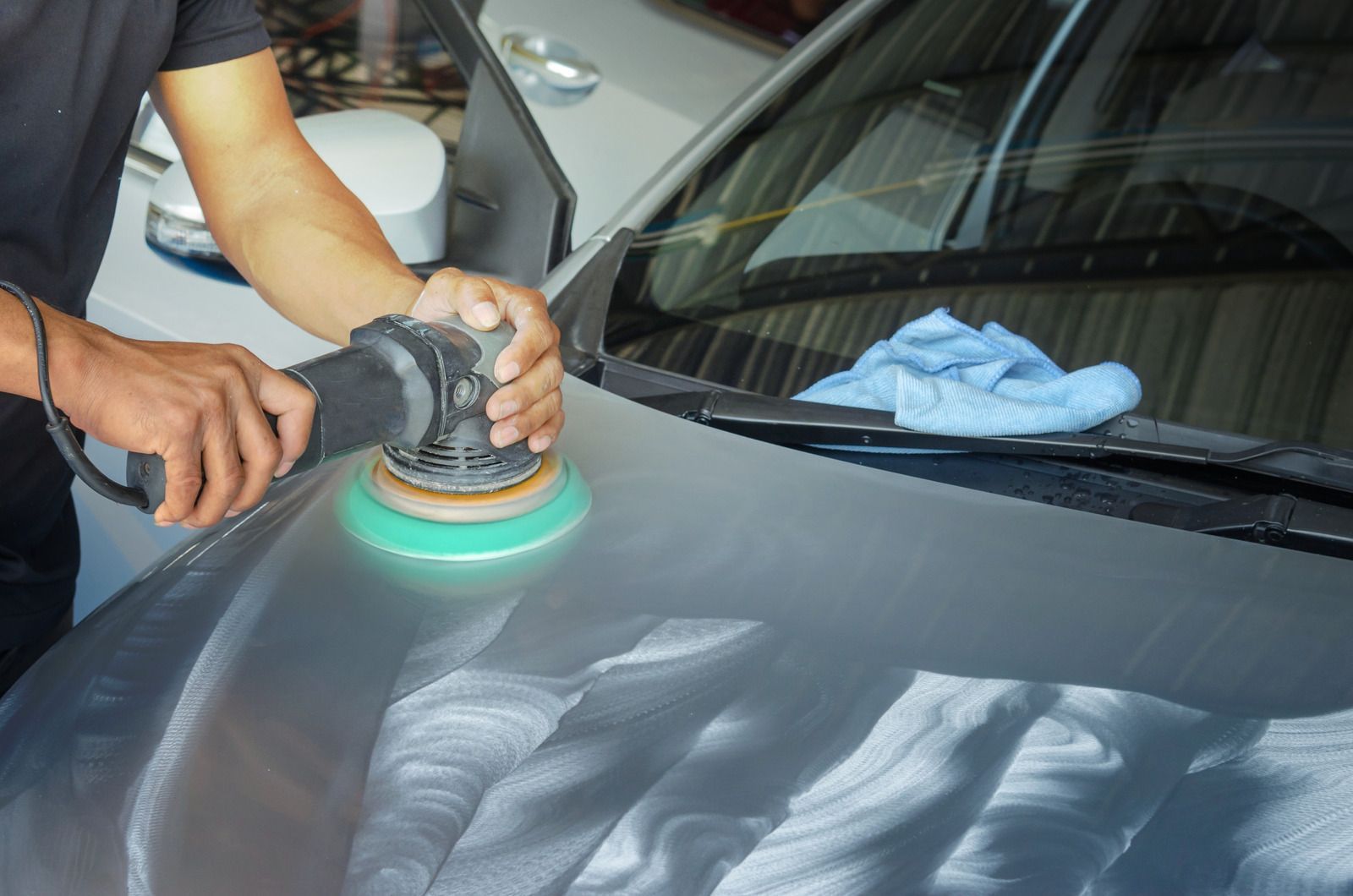 A man is polishing the hood of a car with a machine.