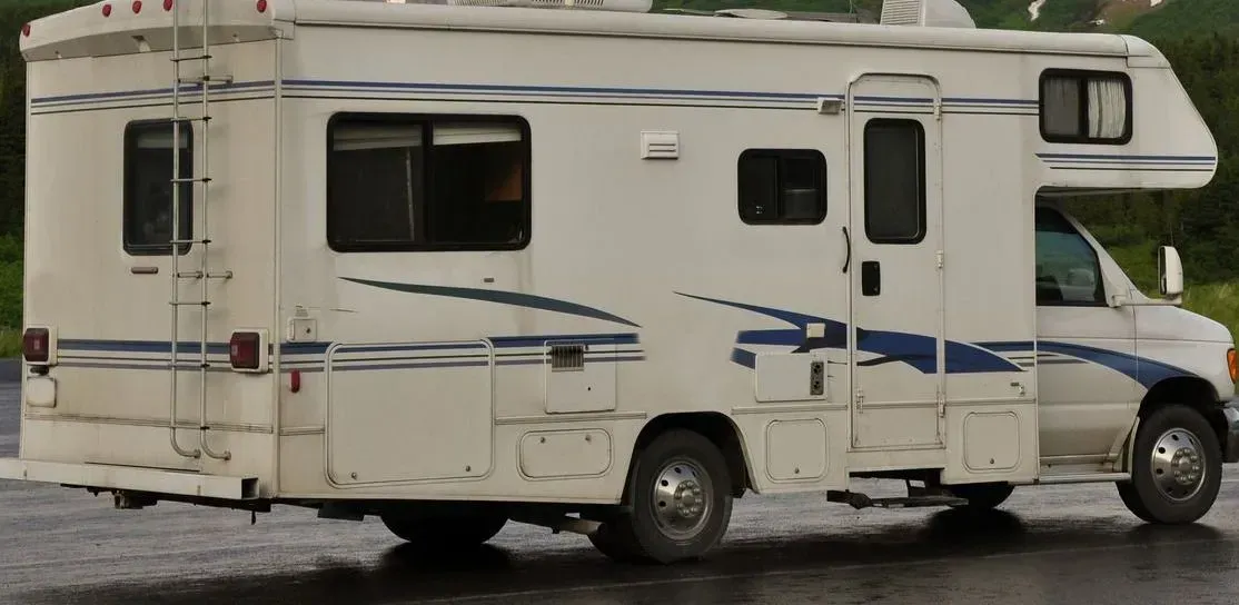 A white rv with blue stripes is parked in the rain