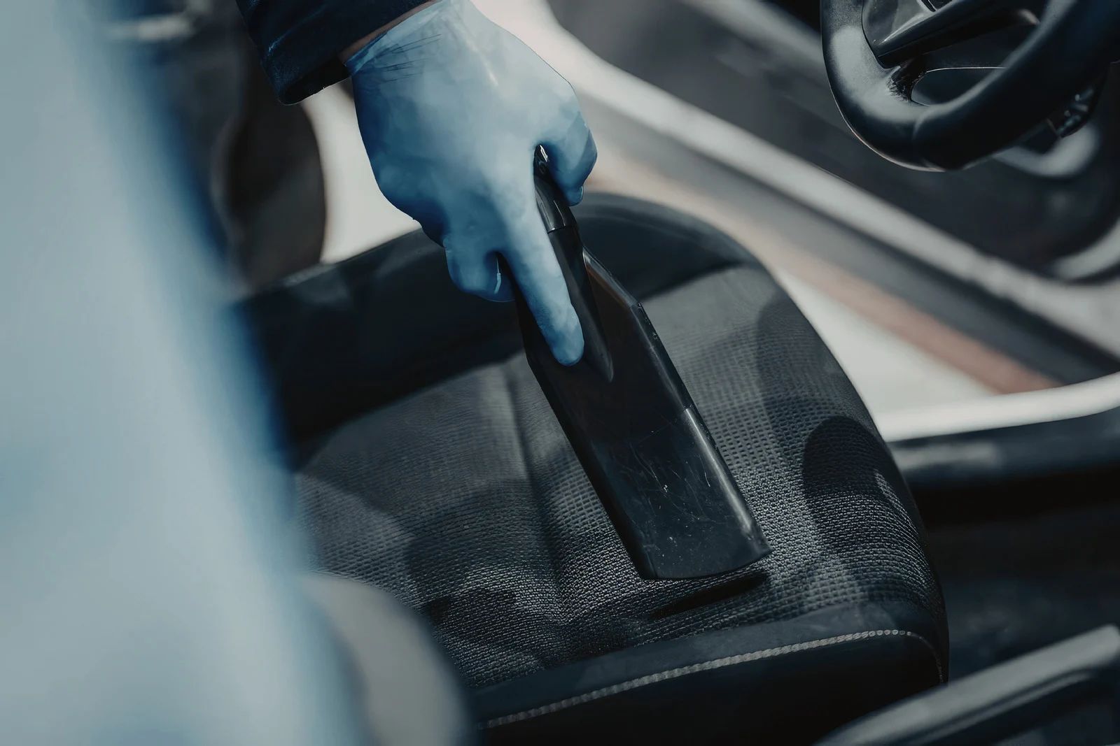 Gloved hand wiping a car seat with a cleaning cloth inside a vehicle