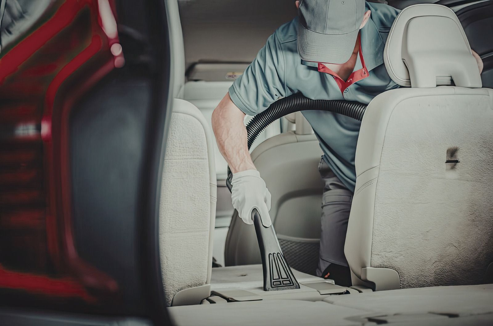 Person vacuuming a car interior with a handheld cleaner, beige seats and floor visible