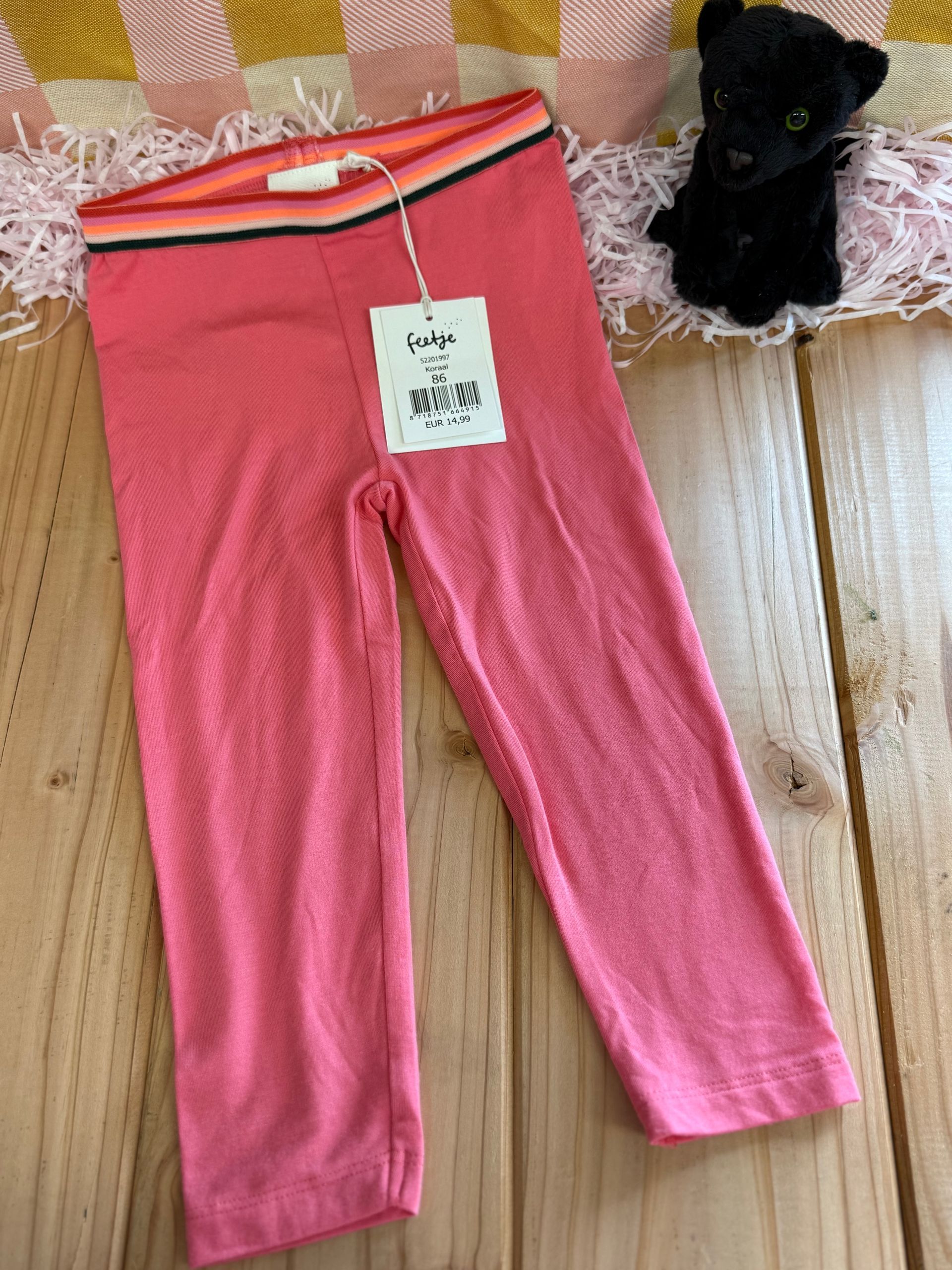 Op een houten tafel liggen een paar roze leggings naast een knuffeldier.