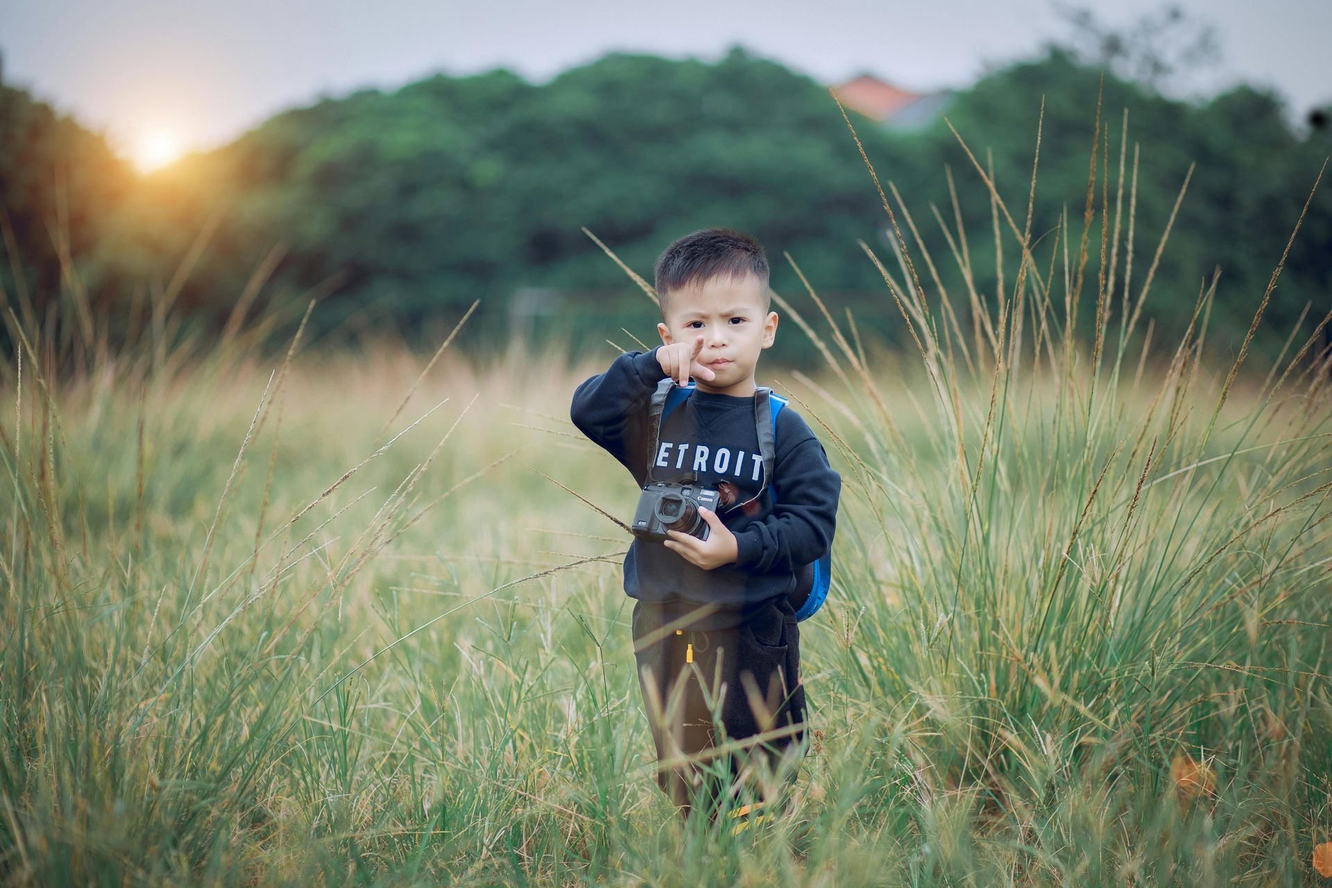 Een jonge jongen staat in een veld met een camera in zijn hand.